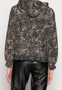 Sudadera con capucha de color gris oscuro con un patrón abstracto en rosa. Presenta mangas largas y un dobladillo acanalado. Combinada con pantalones de cuero negros.