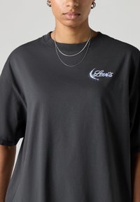 Camiseta de algodão preta com mangas curtas, corte descontraído e logótipo "Levi's" azul salpicado no lado esquerdo do peito.