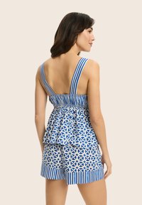 Niebieska i biała top z peplum w wzory, z szerokimi paskami, marszczoną talią i pasującymi spodniami w wzory, na neutralnym tle.