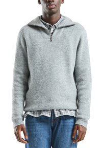 Szary prążkowany sweter z dzianiny, z półzamkniętym kołnierzem na zamek, noszony na koszuli w kratę. Posiada długie rękawy i luźny krój.