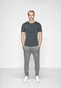 Grå t-shirt med korte ærmer med et sort bison grafik, parret med grå sweatpants og hvide sneakers. Simpelt, afslappet design.