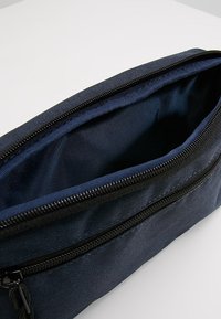 Mörkblå tygpenna med svart dragkedja. Rektangulär form, texturerad yta, insidan kl ädd med slät tyg, minimal design.