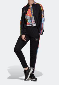 Black athletic tracksuit featuring a colorful graphic design on the shirt, with stripes on the sleeves and iconic logo on pants.
