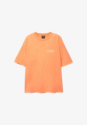 Orange cotton T-shirt with a loose fit, short sleeves, and a rounded neckline. Features white scripted logo on the front.