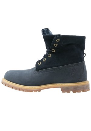 Sort læder- og ruskindsnæbel støvle med tanfarvet gummisål og metaløjer, Timberland-logo på hælen, sidevisning.