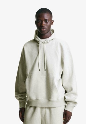 Hellgrauer Hoodie aus weichem Material mit einer Fronttasche, Kapuze mit Kordelzug und gerippten Bündchen. Getragen mit passenden hellgrauen Hosen.