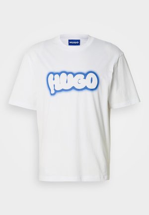 T-shirt de algodão branca com um grande logotipo estilizado "HUGO" em azul e branco, mangas curtas, decote redondo e um corte relaxado.