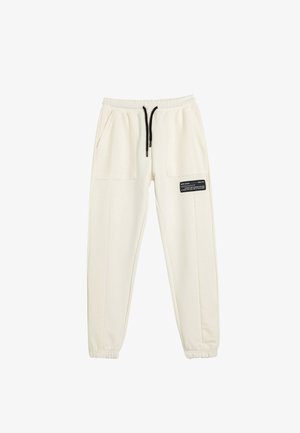 Joggers crema hechos de un tejido suave, con una cintura elástica con cordón, dos grandes bolsillos laterales y un detalle de etiqueta negra.