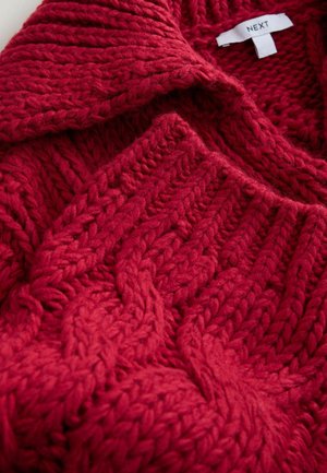Red knitted sweater made of thick yarn, featuring a cable knit design with raised patterns and a soft, textured finish.