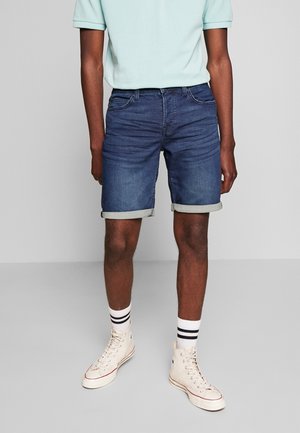 Dunkelblaue Jeansshorts mit Umschlägen und klassischem Fünf-Taschen-Design. Kombiniert mit weißen High-Top-Sneakern und gestreiften Socken.