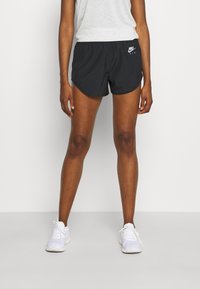 Pantalones cortos deportivos negros con un dobladillo curvo, logo de Nike en el lado izquierdo, cintura elástica, combinados con zapatillas blancas.