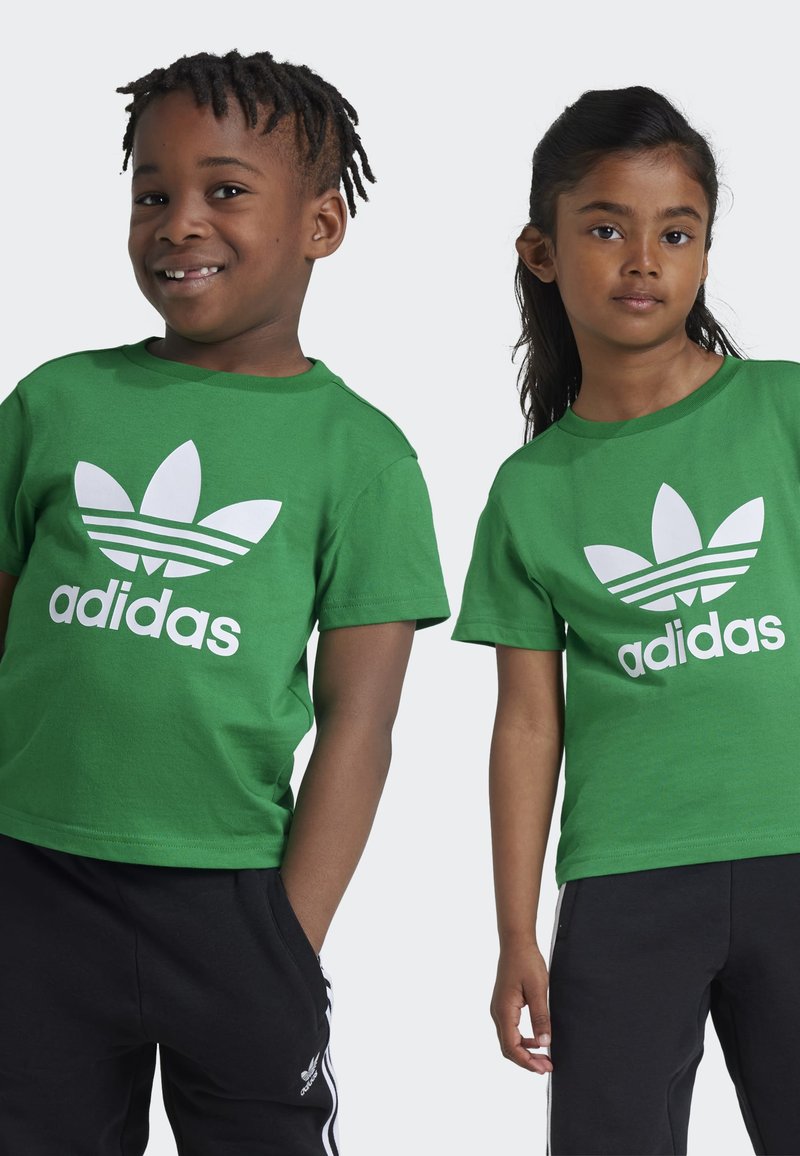 Zelené bavlněné trička s bílým logem Adidas a designem trojlístku, s krátkými rukávy a kulatými výstřihy, kombinované s černými kalhotami.