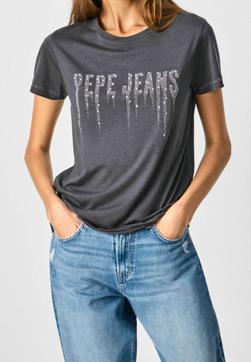 Dark gray cotton t-shirt with short sleeves, featuring the text "PEPE JEANS" in silver rhinestones, relaxed fit, worn with light blue jeans.