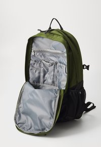 Sac à dos vert et noir avec un intérieur gris ; doté de plusieurs poches, d'un compartiment zippé et de poches latérales en maille.