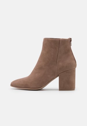 Bottine en daim marron avec talon bloc et fermeture éclair au dos, bout pointu, texture lisse, présentée sur un fond clair uni.