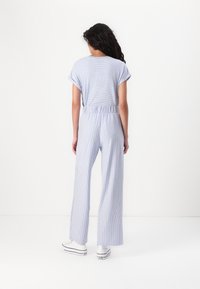 Lätt randig jumpsuit i blått och vitt; korta ärmar, elastisk midja, vida ben, ihop med vita sneakers.