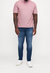 Kortärmad, ljusrosa polo med krage och logotyp, kombinerad med slim-fit blå jeans och vita sneakers, som visar en avslappnad stil.