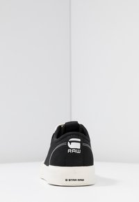 Baskets en toile noires avec une semelle en caoutchouc blanc. Dotées d'un onglet arrière et du logo "RAW" en blanc. Design épuré, accents de couture minimalistes.