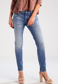 Ljusblå smala jeans med en blekt tvätt, med fem fickor och dragkedja. Tyget har en slät textur. Bärs med beige plattformsskor.