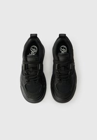 Mustad musta värvi spordijalatsid, millel on sile tekstuur, ümar nina ja nöörid. Omab pehmendatud kaelaosa ja bränditud sisenemist, millel on diskreetsed disainielemendid.