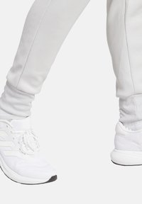 Weiße Sporthosen aus strukturiertem Material mit eng anliegenden Bündchen, kombiniert mit weißen Laufschuhen mit einem Obermaterial aus Mesh und einer Gummisohle.