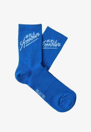 Par med knallblå crew-sokker med hvit "Hotel Amour"-tekst på mansjettene og "SELECTED"-tekst på fotbuen.