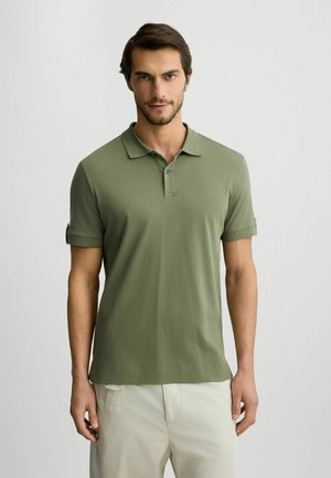 Olive green polo shirt with a classic collar, short sleeves, two buttons, and a small logo on the chest. Made from soft cotton fabric.