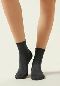 Schwarze Knöchelsocken mit einem glänzenden, metallischen Fadenmuster. Weicher, elastischer Stoff mit passgenauem Design und geripptem Bündchen.