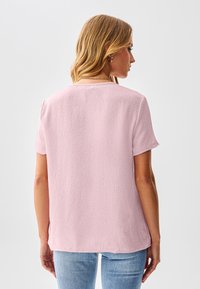 Korte mouwen top in lichtroze, met een gestructureerde stof en een ontspannen pasvorm. Detail aan de achterkant van de hals en lichte zijsplitten. Draagt mooi bij denim.