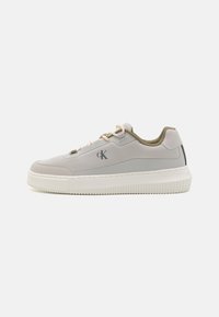 Scarpa sportiva grigia chiara con una texture liscia, suola di gomma bianca, lacci beige e un marchio sottile. Presenta un design low-top e un colletto imbottito.