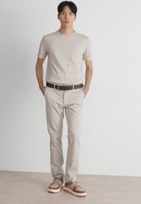 T-shirt ajustée beige clair, pantalon blanc cassé, ceinture en cuir marron et baskets à accents marron. Texture en coton lisse, design décontracté.