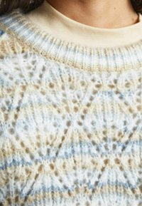 Pull en maille à motif géométrique en crème, beige et bleu clair, avec une surface texturée et un col côtelé.
