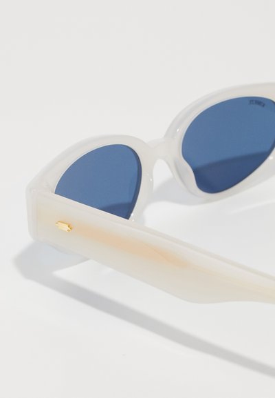 Translucent white sunglasses with rounded blue lenses. The arms feature a gold accent and a gradient fade from white to light orange.