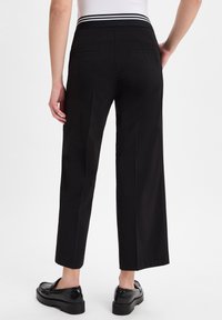 Zwarte wijde broek met een hoge taille, voorzien van een gestreepte elastische tailleband, achterzakken en een gladde stoftextuur. Chunky zwarte schoenen.