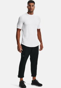 Maglietta sportiva bianca e pantaloni neri aderenti. La maglietta ha maniche corte e scollo rotondo. I pantaloni presentano tasche laterali e zip alle caviglie.