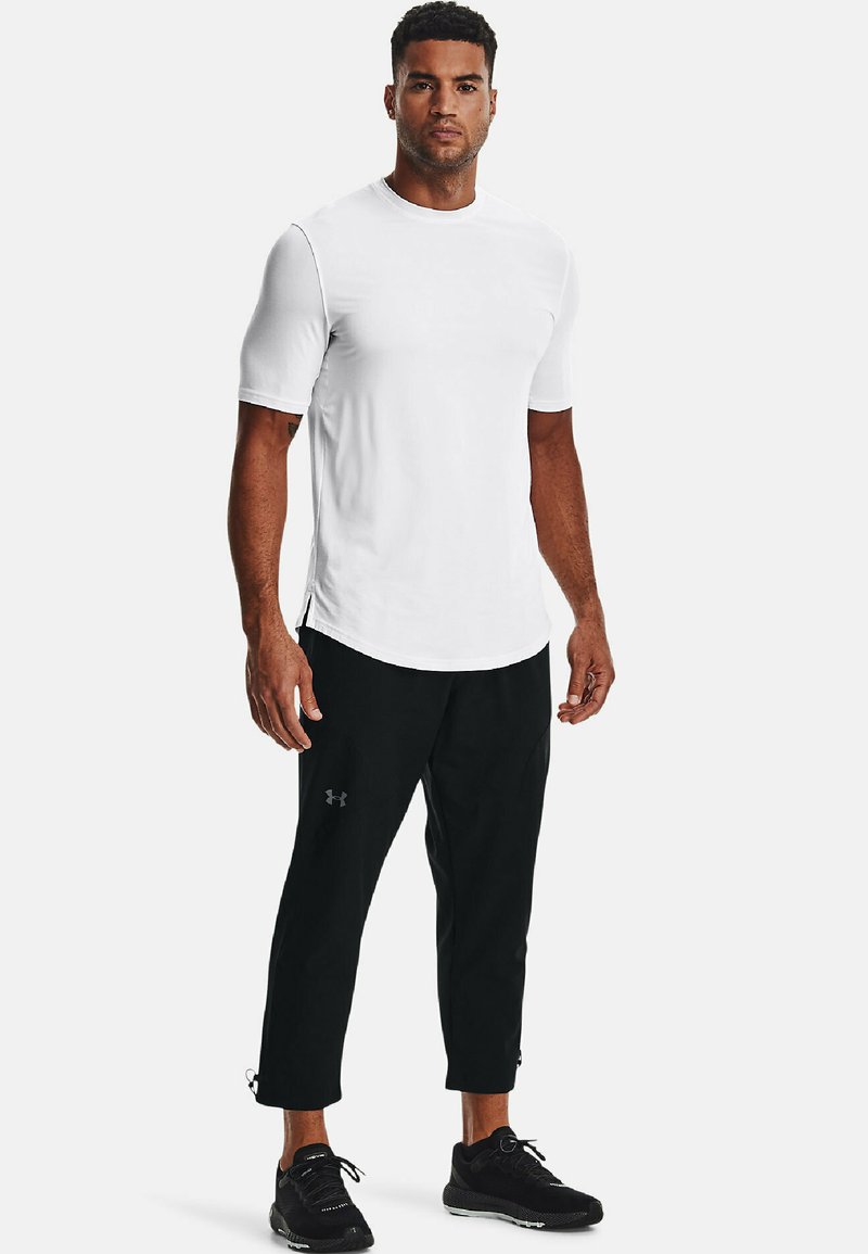 Maglietta sportiva bianca e pantaloni neri aderenti. La maglietta ha maniche corte e scollo rotondo. I pantaloni presentano tasche laterali e zip alle caviglie.