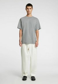 Szary T-shirt z krótkim rękawem zestawiony z białymi, luźnymi spodniami i czarnymi butami. Prosty design o swobodnej sylwetce.