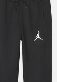 Black sweatpants with an elastic waistband, drawstring, side pockets, and a white Jumpman logo on the left leg. Smooth texture.