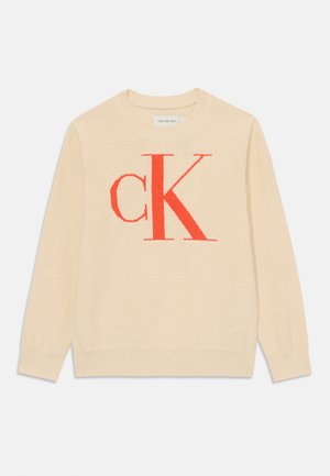 Pull léger beige en tissu doux, comportant un grand logo rouge "CK" au centre, col rond et poignets côtelés.