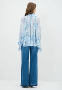 Lyseblå blomsterbluse med bløde ærmer, der er snøret ind ved håndleddene; parret med høj lavede, vide denimjeans.