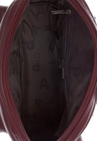 Interior de un bolso de cuero burdeos que muestra un amplio compartimento principal con un forro de tela y un bolsillo con cremallera.
