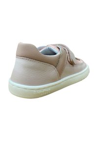 Zapatilla de cuero beige con una correa de velcro, parte superior texturizada, forma redondeada y suela de goma blanca. Marca en el lateral cerca del talón.
