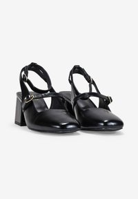 Talons hauts slingback en cuir noir avec un bout carré, une bride de cheville et un talon bloc. Présente un accent en boucle dorée sur la bride.