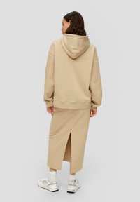 Kapuchega beež sweatshirt koos sobiva midi seeliku, millel on taga lõhik. Kandetuna valgete tossude ja ribakonstruktsiooniga sukavarrastega.