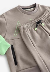 Grau Sweatshirt- und Jogginghosen-Set mit hellgrünen Akzenten. Enthält eine Reißverschlusstasche und große grüne Buchstaben auf der Vorderseite. Weiches, strukturiertes Material.
