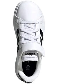 Zapatilla deportiva blanca con rayas negras, presenta un cierre con cordones y una correa de Velcro. Construida de material sintético y tejido texturizado.