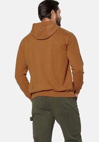 Brauner Baumwoll-Hoodie mit Kordelzugkapuze, gerippten Bündchen und Saum. Kombiniert mit olivgrünen Cargohosen mit Seitentaschen.