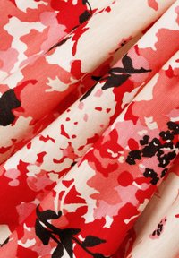 Floral fabric with varying shades of red, pink, and cream, featuring a smooth texture and a design of large abstract flowers and leaves.