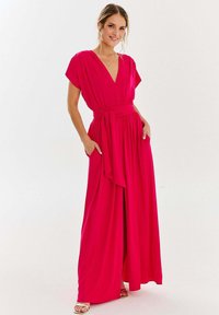 Fuksjowa sukienka maxi z głębokim dekoltem w literę V, krótkimi rękawami i paskiem w talii. Posiada zwiewny materiał i boczne kieszenie. W zestawie klapki.