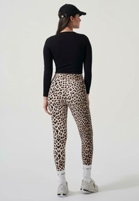 Leggingse s uzorkom leoparda s pripijenim dizajnom, napravljene od rastezljivog materijala, u kombinaciji s crnom majicom dugih rukava i crnom kapom.